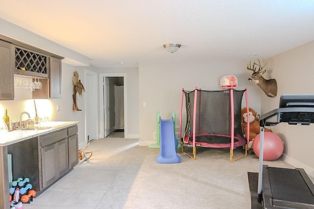 exercise room featuring light colored carpet, wet bar, baseboards, and a sink