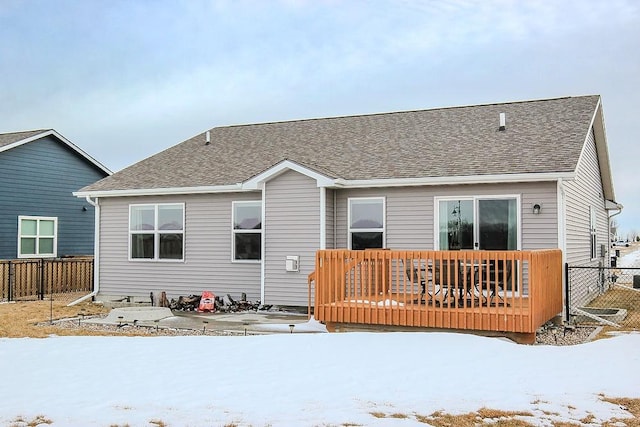 snow covered property featuring a wooden deck, fence, and a shingled roof