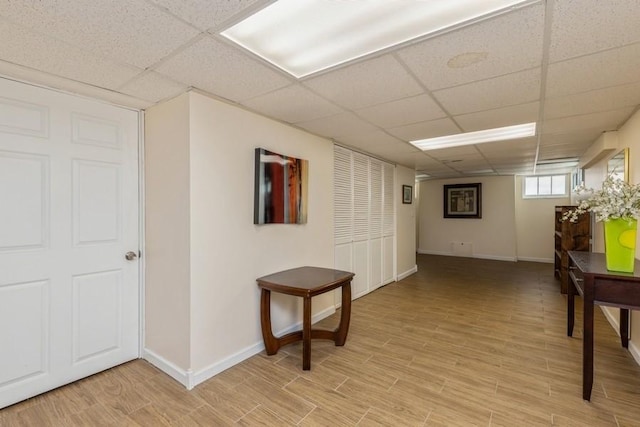 corridor with baseboards, a paneled ceiling, and light wood-style flooring