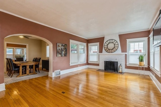 living room featuring light wood-type flooring, visible vents, arched walkways, a fireplace, and baseboards