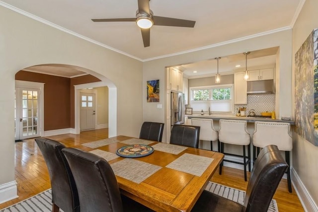 dining area featuring crown molding, baseboards, arched walkways, and light wood finished floors