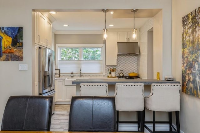 kitchen featuring a breakfast bar, under cabinet range hood, a sink, stainless steel fridge with ice dispenser, and decorative backsplash