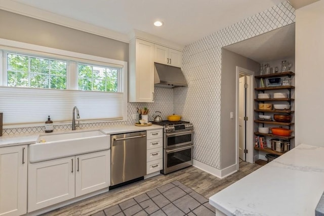 kitchen with light wood-type flooring, under cabinet range hood, a sink, stainless steel appliances, and wallpapered walls