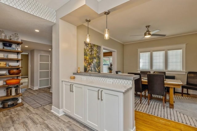 kitchen featuring a peninsula, ornamental molding, pendant lighting, white cabinetry, and light wood-type flooring