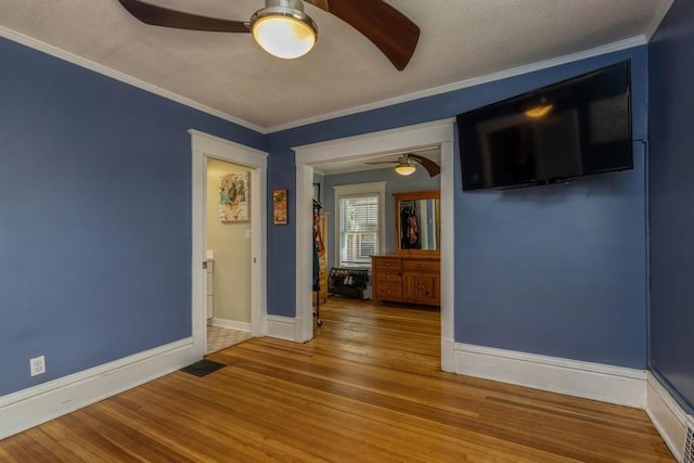 spare room with baseboards, crown molding, a ceiling fan, and wood finished floors