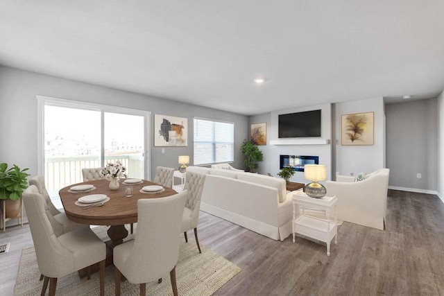 dining area with a glass covered fireplace, baseboards, wood finished floors, and recessed lighting