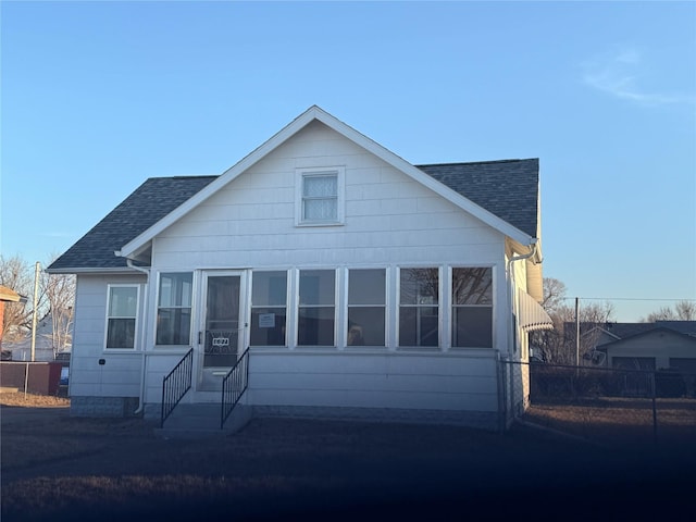 bungalow-style house featuring a sunroom, fence, roof with shingles, and entry steps