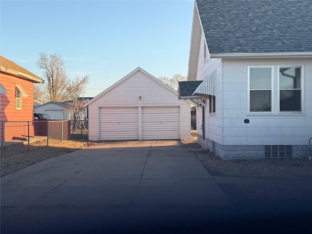 view of side of property featuring a detached garage, an outbuilding, roof with shingles, and fence