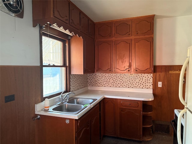 kitchen with wooden walls, a wainscoted wall, light countertops, freestanding refrigerator, and a sink