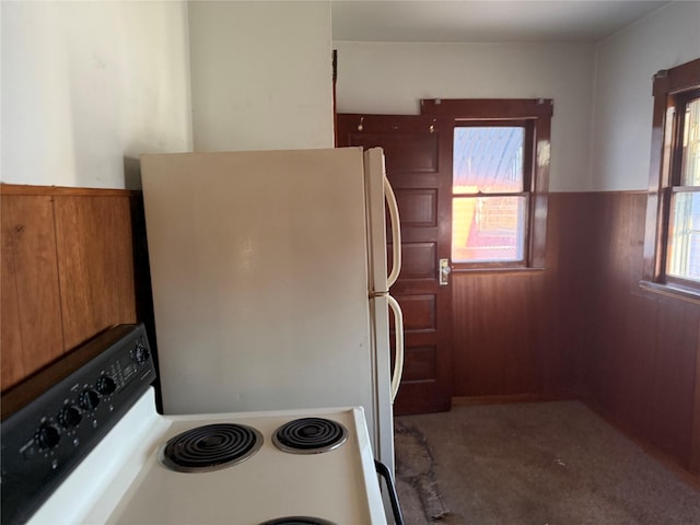 kitchen featuring brown cabinetry, a wainscoted wall, freestanding refrigerator, electric stove, and wood walls