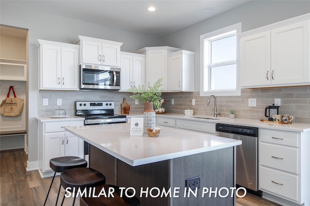 kitchen with a center island, light countertops, white cabinets, stainless steel appliances, and a sink