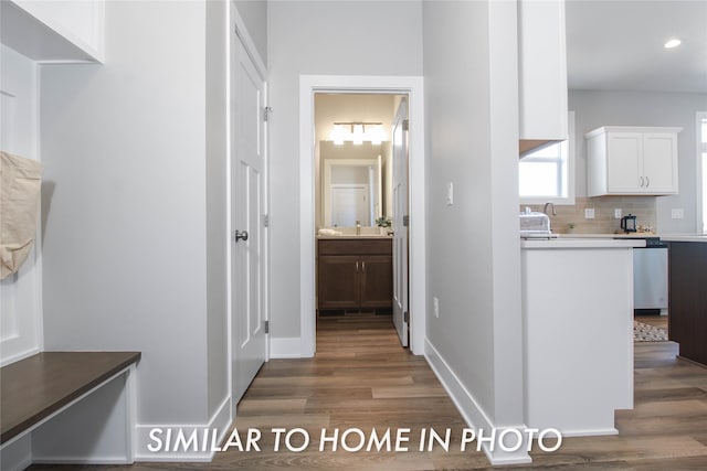 hallway featuring recessed lighting, wood finished floors, baseboards, and a sink