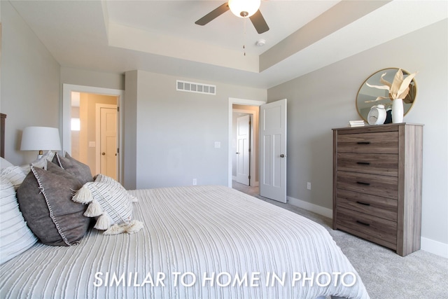 bedroom with visible vents, light carpet, a ceiling fan, a tray ceiling, and baseboards