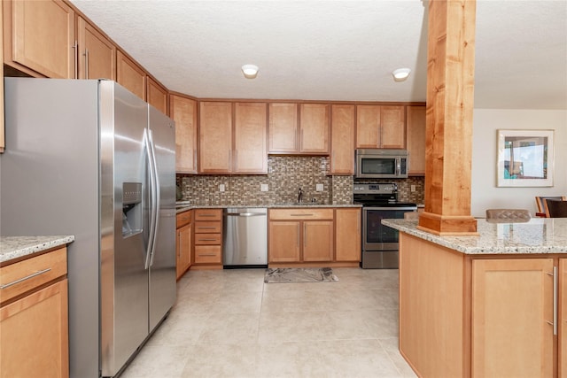 kitchen featuring decorative columns, light stone counters, decorative backsplash, stainless steel appliances, and a sink