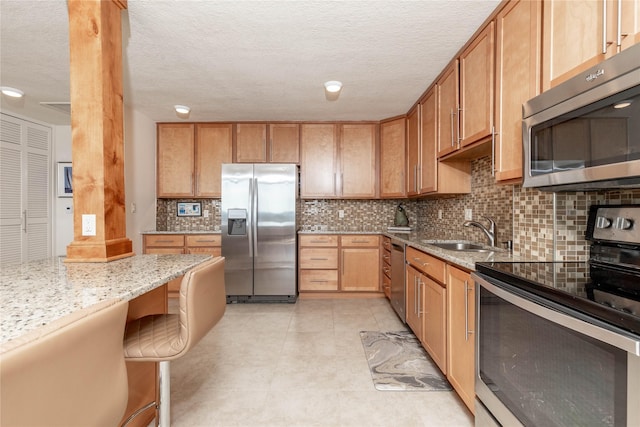 kitchen featuring backsplash, light stone countertops, light tile patterned floors, stainless steel appliances, and a sink