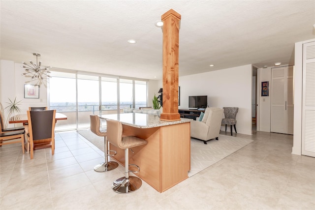 kitchen with a textured ceiling, a center island, a wall of windows, decorative columns, and light stone countertops