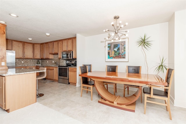 kitchen with light stone countertops, appliances with stainless steel finishes, pendant lighting, a notable chandelier, and backsplash