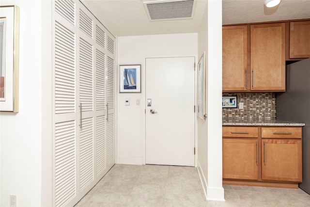 interior space with visible vents, brown cabinets, light stone counters, freestanding refrigerator, and decorative backsplash