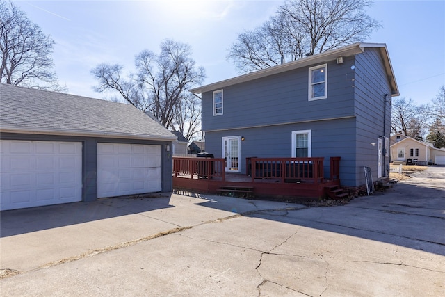 back of house with a deck, an outbuilding, a garage, and a shingled roof