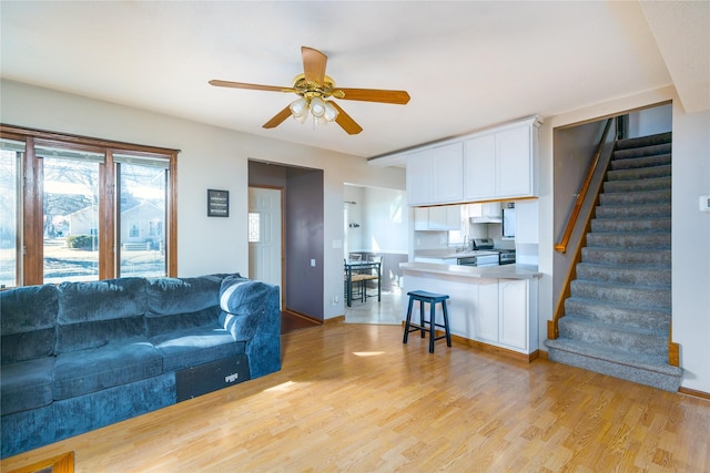 living area with stairs, light wood-type flooring, and a ceiling fan