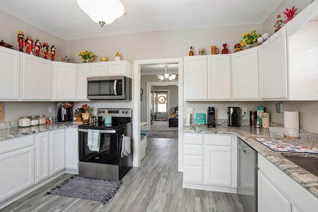 kitchen featuring light stone counters, stainless steel appliances, light wood-style floors, white cabinets, and a chandelier