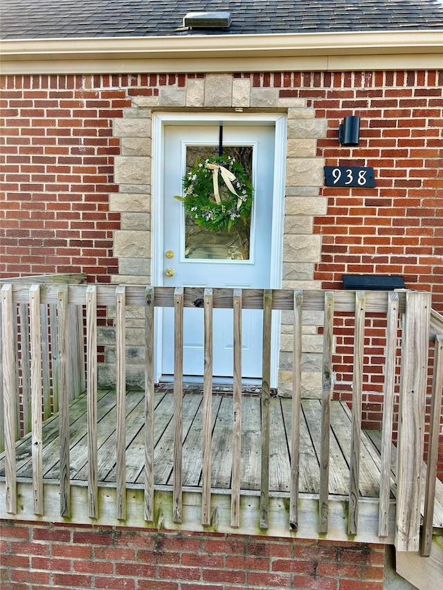 entrance to property featuring brick siding and a shingled roof