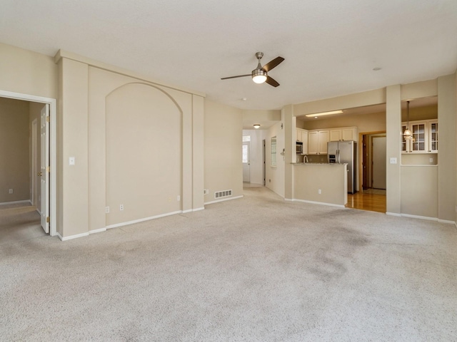 unfurnished living room with visible vents, light colored carpet, baseboards, and a ceiling fan