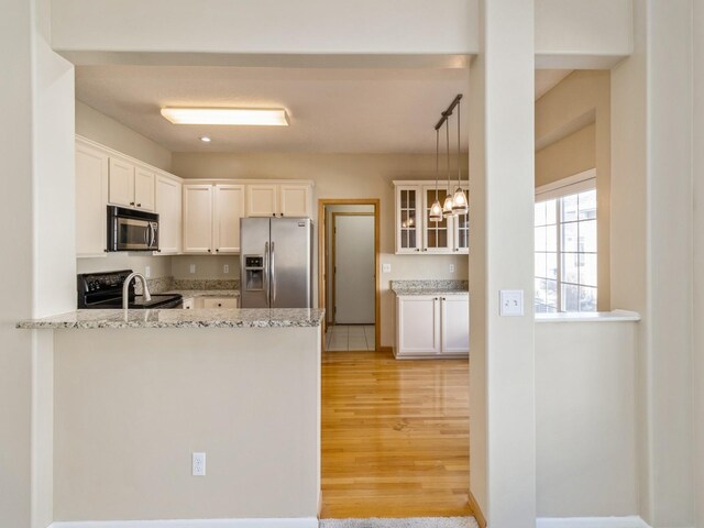 kitchen featuring a peninsula, stainless steel appliances, glass insert cabinets, white cabinetry, and light wood-type flooring