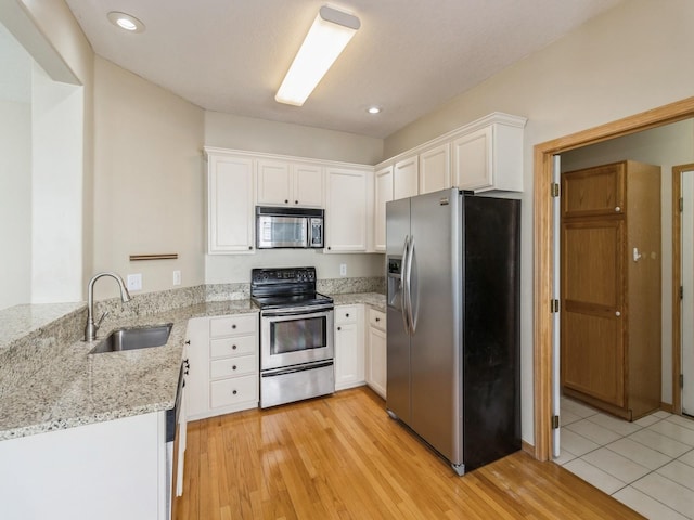 kitchen with a sink, light stone counters, light wood-style floors, appliances with stainless steel finishes, and white cabinets