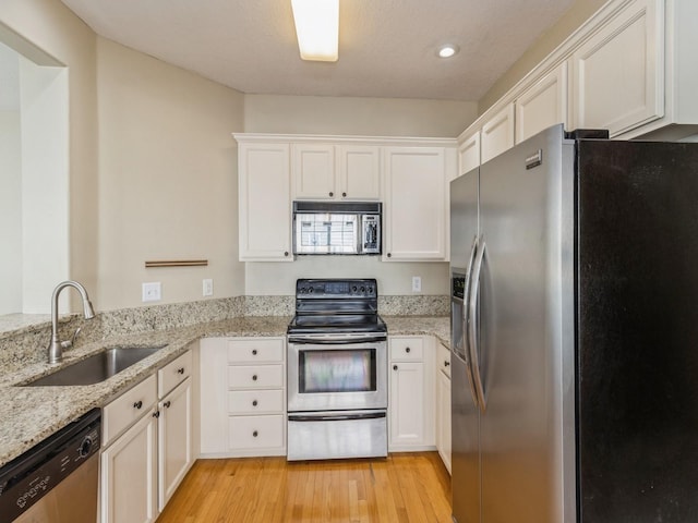 kitchen featuring light wood finished floors, light stone counters, appliances with stainless steel finishes, white cabinets, and a sink