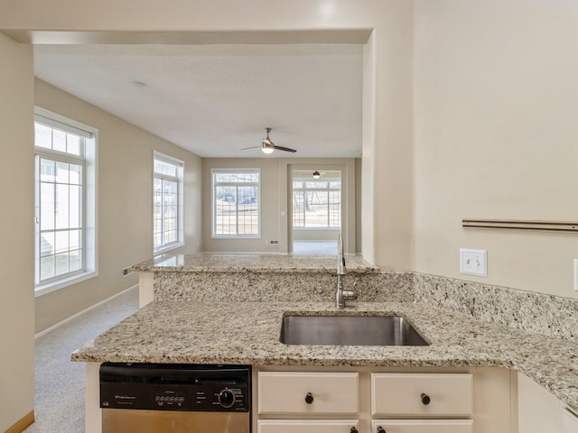 kitchen featuring a sink, a peninsula, white cabinets, light stone countertops, and dishwasher