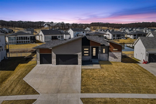 view of front of house featuring fence, an attached garage, stone siding, a lawn, and a residential view