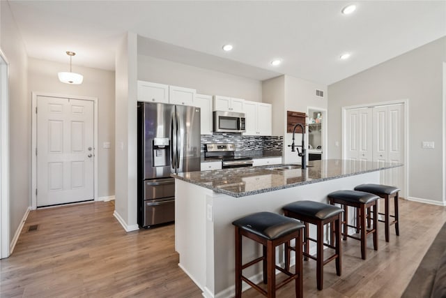 kitchen featuring a kitchen bar, a sink, white cabinetry, stainless steel appliances, and decorative backsplash