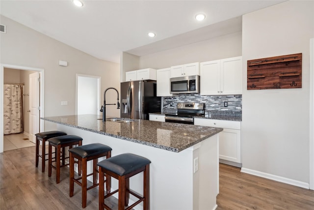 kitchen with tasteful backsplash, white cabinets, stainless steel appliances, and a kitchen bar