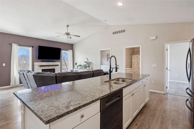 kitchen featuring visible vents, a sink, black dishwasher, a warm lit fireplace, and light wood finished floors