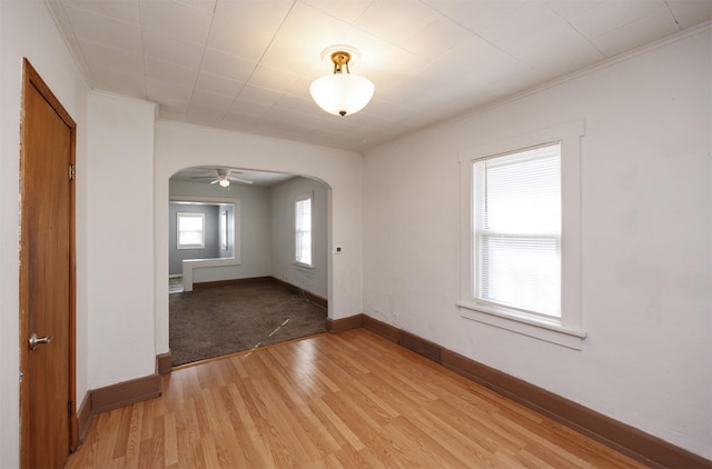 spare room with ornamental molding, baseboards, arched walkways, and light wood-type flooring