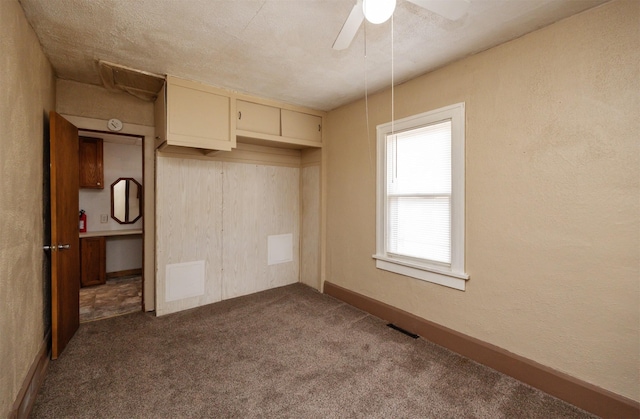 unfurnished bedroom with a textured wall, baseboards, dark carpet, and ceiling fan