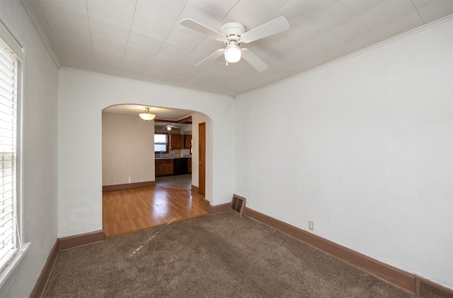 carpeted spare room featuring visible vents, a ceiling fan, arched walkways, crown molding, and baseboards