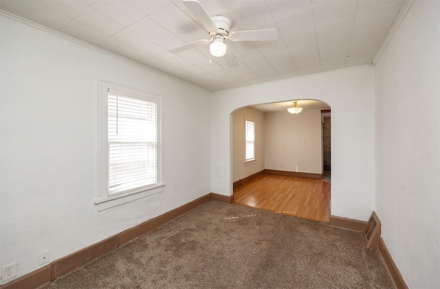 carpeted spare room with arched walkways, baseboards, ceiling fan, and ornamental molding