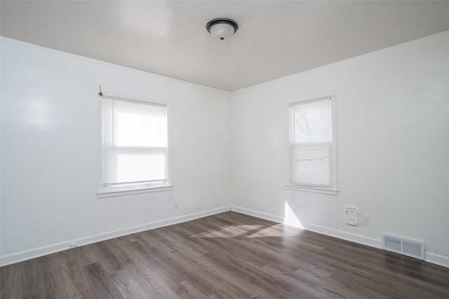 empty room featuring visible vents, dark wood-type flooring, and baseboards