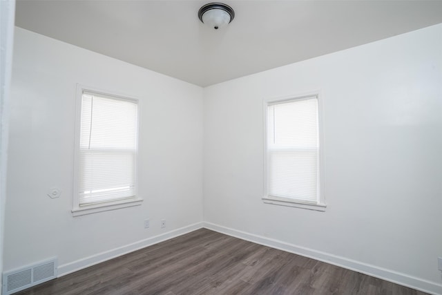 empty room featuring dark wood finished floors, visible vents, plenty of natural light, and baseboards