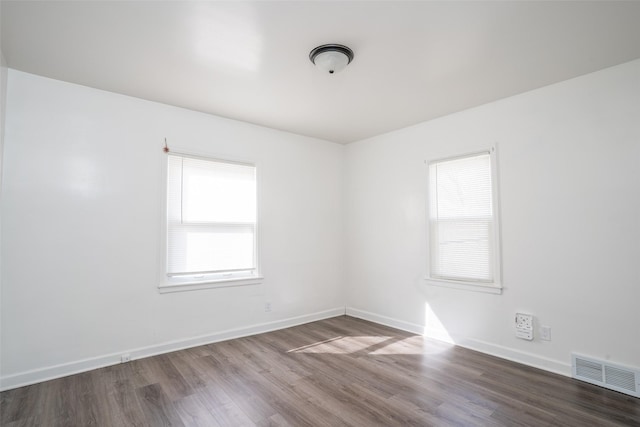 empty room with dark wood finished floors, baseboards, visible vents, and a wealth of natural light