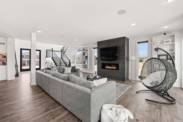 living room featuring visible vents, wood finished floors, recessed lighting, a large fireplace, and stairs