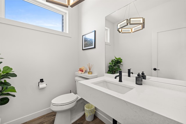 half bath featuring toilet, wood finished floors, baseboards, and a sink