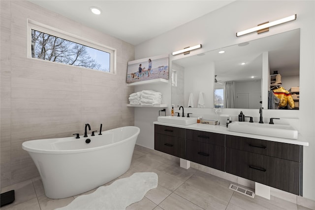 bathroom featuring double vanity, a freestanding tub, visible vents, and a sink