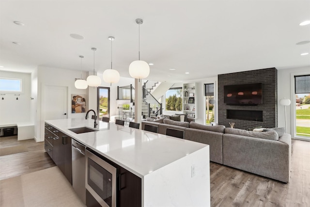 kitchen featuring a sink, light wood-style floors, light countertops, an island with sink, and built in microwave