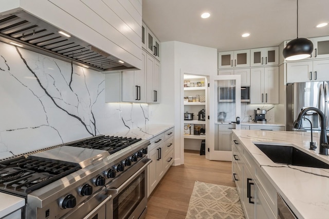 kitchen featuring light stone countertops, light wood-type flooring, custom range hood, appliances with stainless steel finishes, and a sink