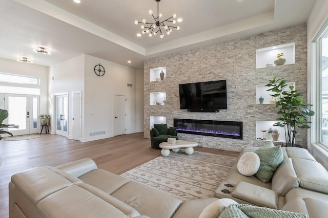 living room featuring a glass covered fireplace, a tray ceiling, visible vents, and wood finished floors