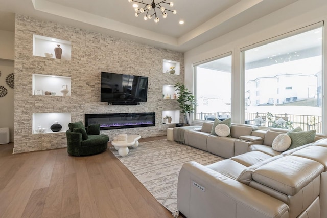 living area with a tray ceiling, wood finished floors, a notable chandelier, and a glass covered fireplace