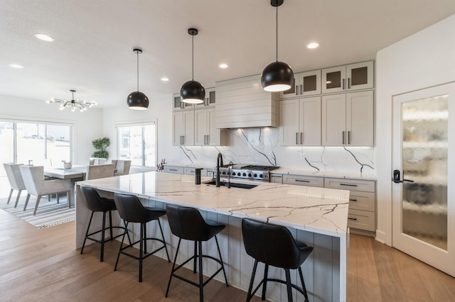 kitchen featuring tasteful backsplash, an island with sink, light wood-style flooring, custom exhaust hood, and a sink